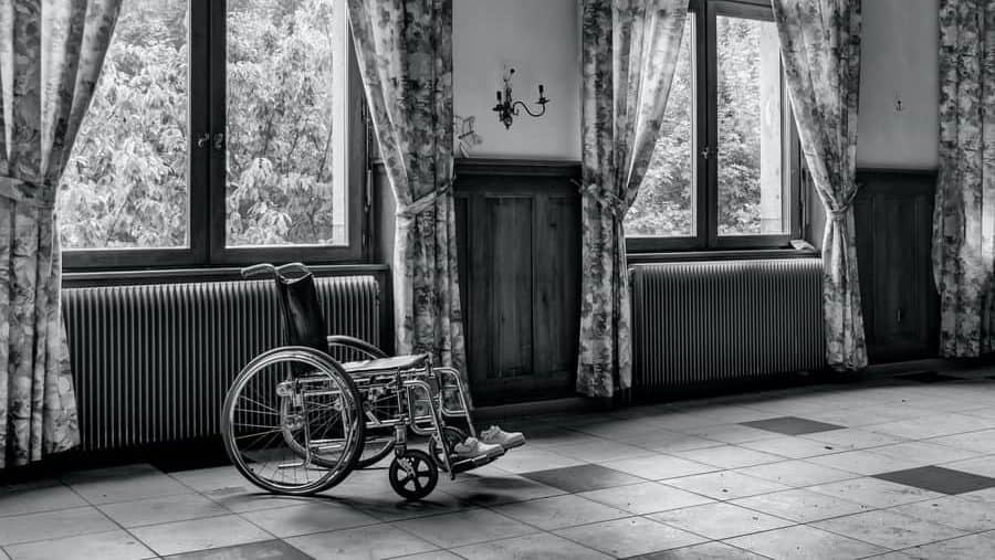 Black and white picture of an empty wheelchair in an empty room. 