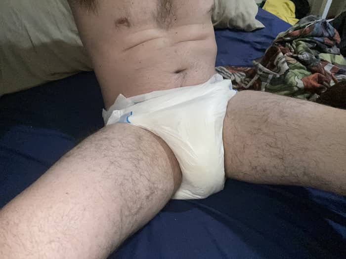 A picture of a man's diapered midsection sitting up in an obviously dry bed thanks to the diaper.